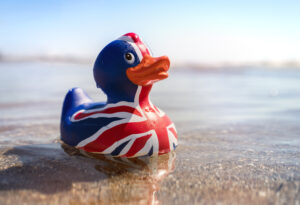 A rubber duck painted with the British Flag sitting on a beach